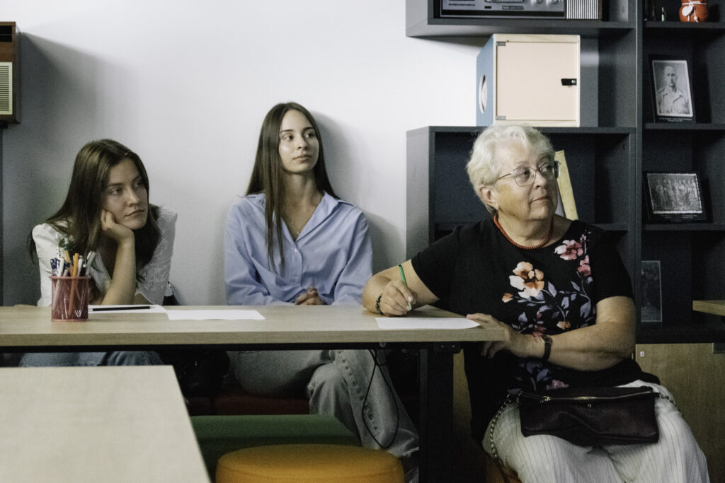 Three women sitting and listening to someone outside of the picture. One of them is taking notes.